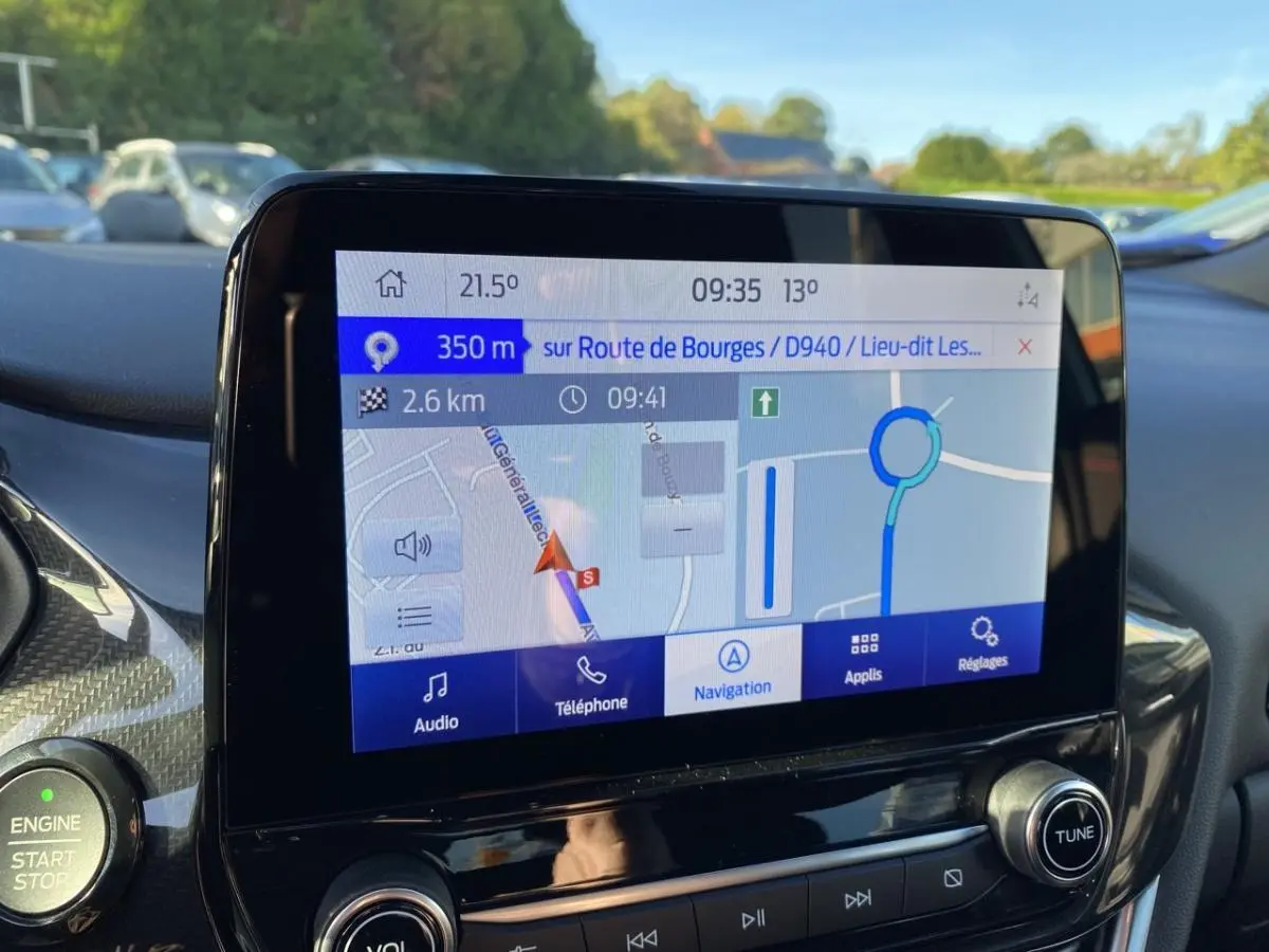 Écran GPS couleur du tableau de bord du Ford Puma gris, avec commandes audio et bouton start/stop visibles.