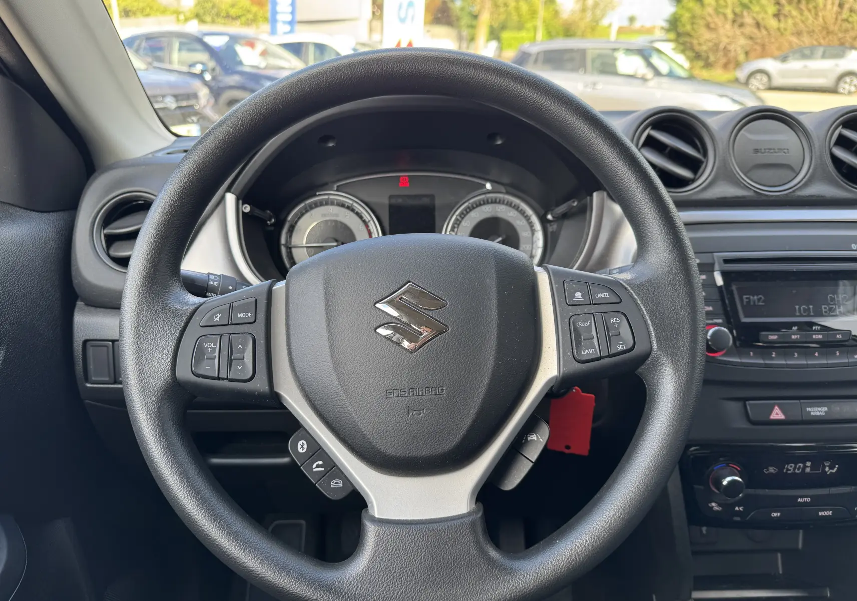 Vue rapprochée du volant noir du Suzuki Vitara blanc 2023, avec commandes intégrées et tableau de bord en arrière-plan.