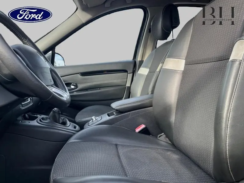 Vue intérieure côté conducteur d'un Renault Grand Scenic noir étoilé, sièges tissu et cuir, volant cuir avec commandes audio.