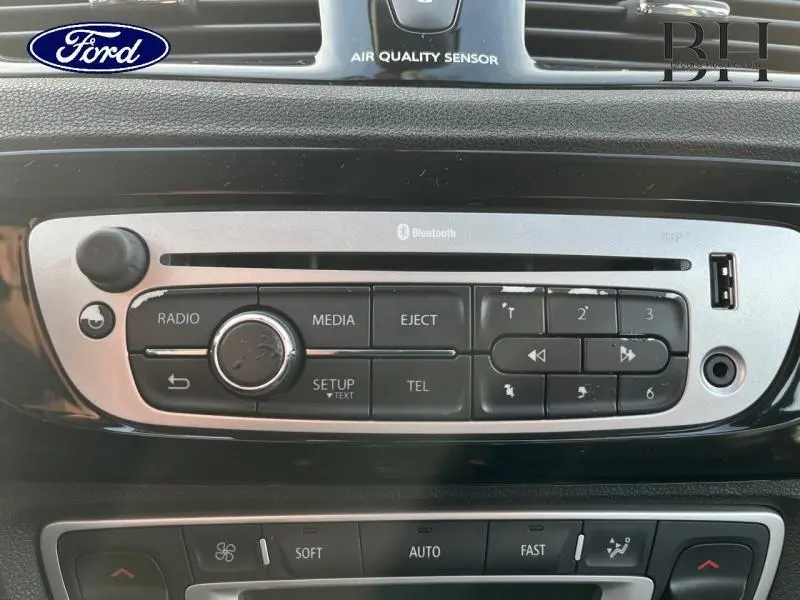 Tableau de bord noir du Renault Grand Scenic 2012, zoom sur la console centrale avec commandes radio et Bluetooth visibles.