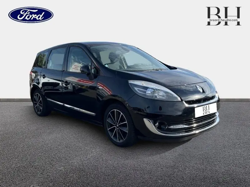 Renault Grand Scenic noir étoilé en 3/4 avant droit, avec jantes alliage et barres de toit visibles.