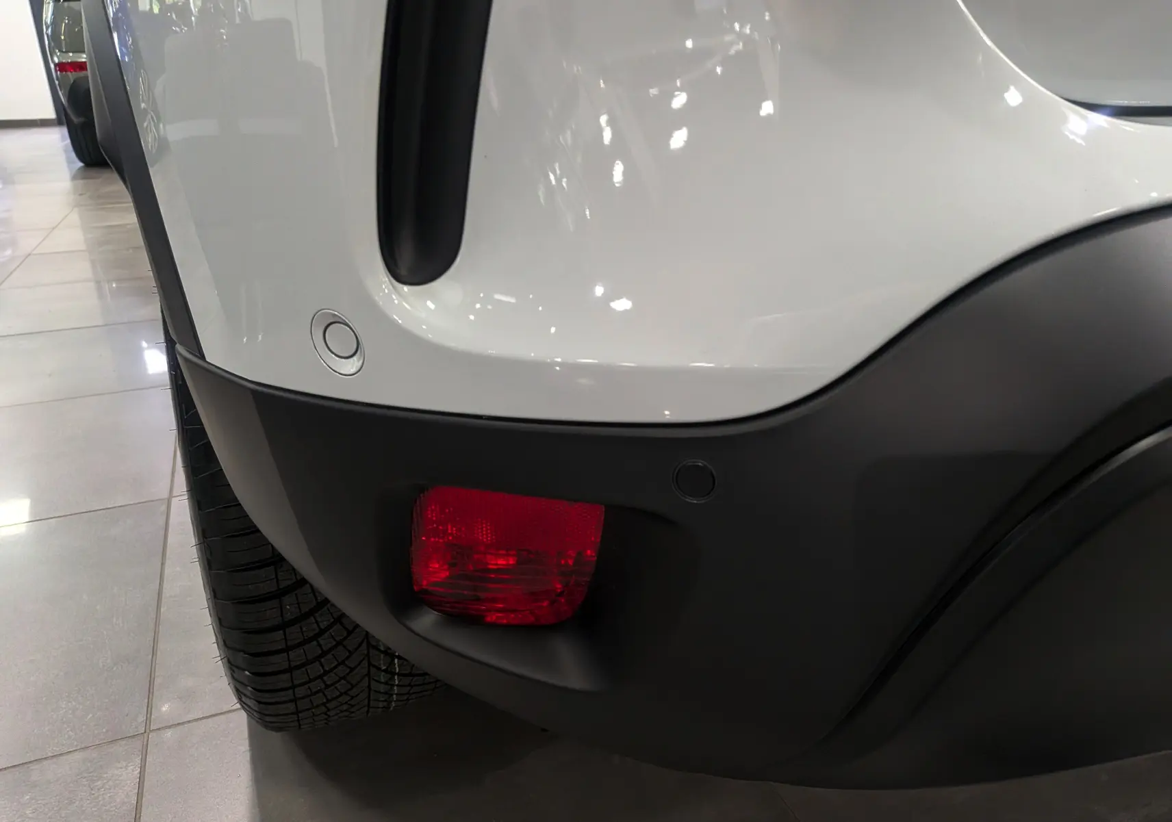 Gros plan sur le feu arrière droit rouge et pare-chocs noir du Citroën C5 Aircross hybride blanc Okénite.
