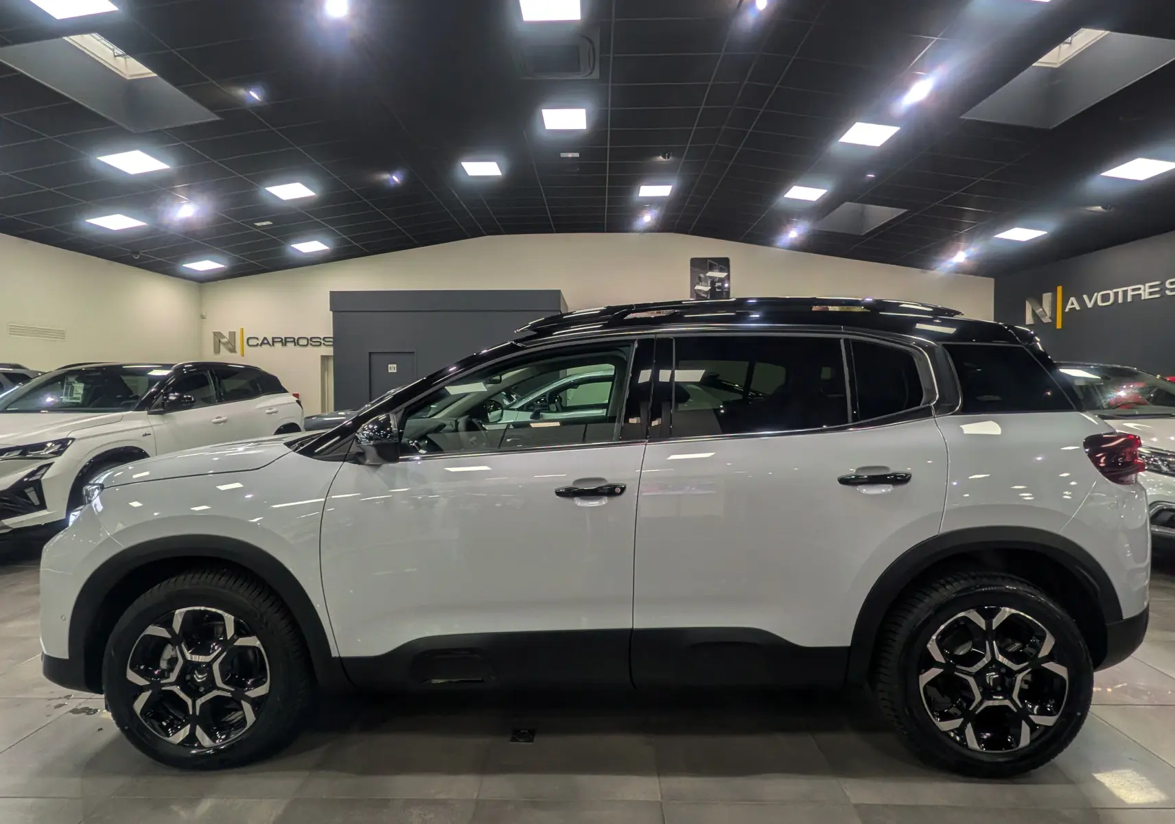 Vue de profil côté gauche d'un Citroën C5 Aircross hybride blanc Okénite avec toit noir en showroom.