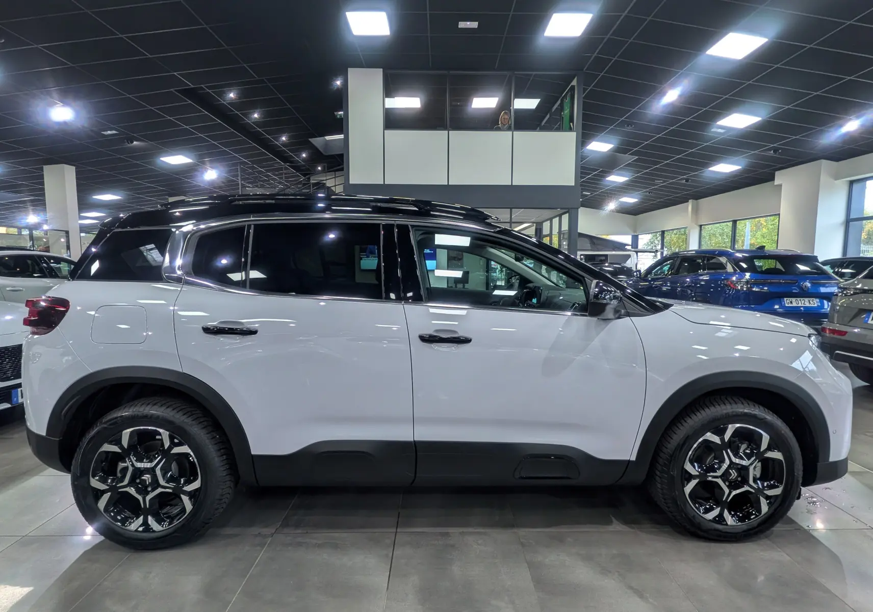 Profil latéral droit d'un Citroën C5 Aircross hybride blanc Okénite avec toit noir dans un showroom lumineux.
