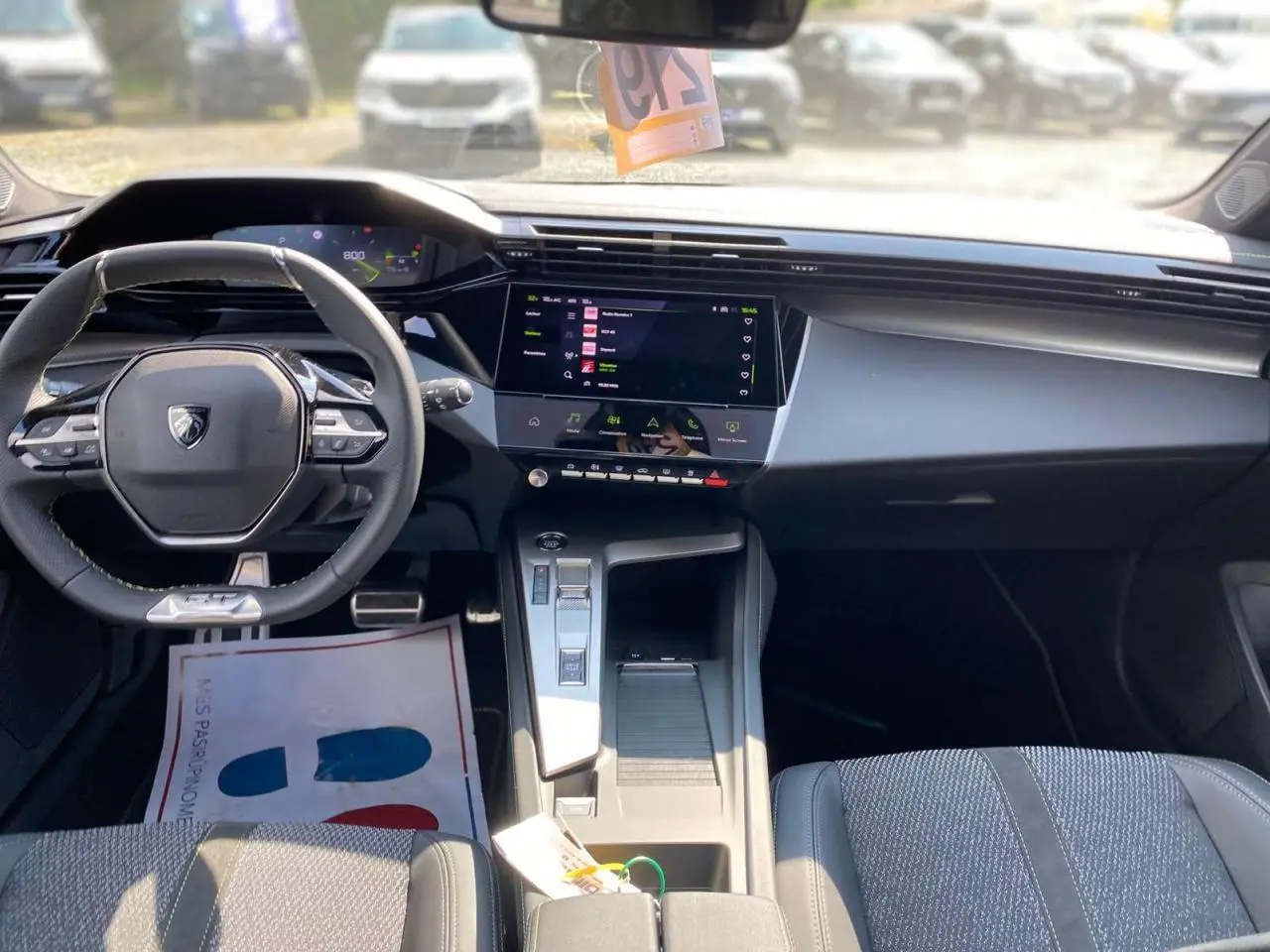 Vue intérieure avant de la Peugeot 308 2025 gris selenium, mettant en valeur le volant compact et l'écran tactile central moderne.