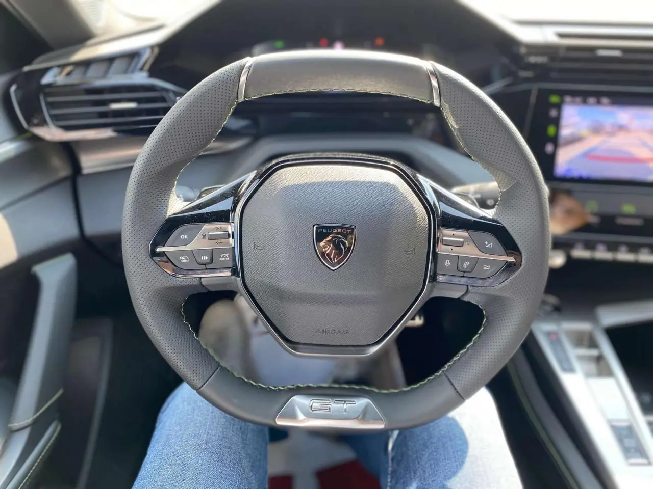 Volant sport GT de la Peugeot 308 2025 en vue plongeante, avec commandes intégrées et coutures vertes visibles.