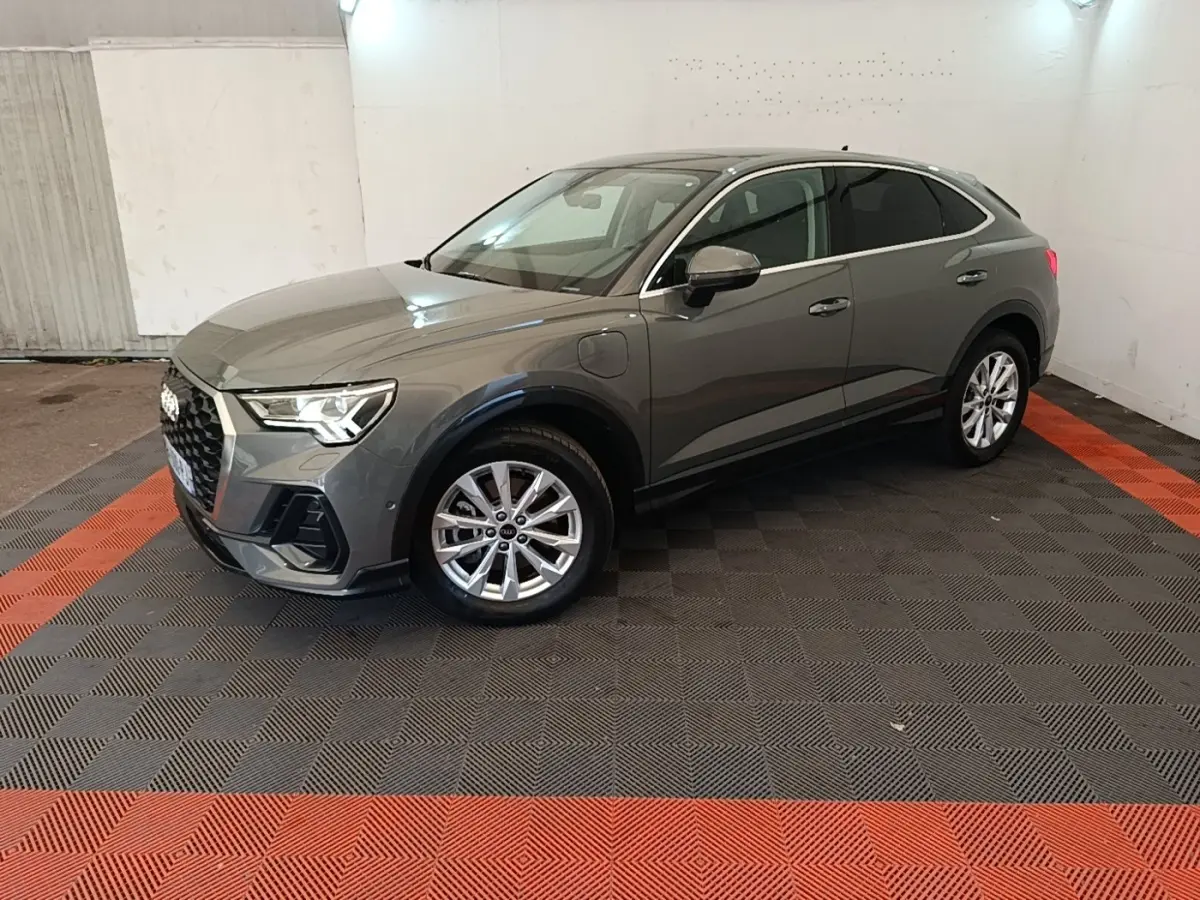 Audi Q3 Sportback hybride rechargeable gris, vue 3/4 avant droit, avec jantes alliage et prise de charge visible sur l'aile avant.
