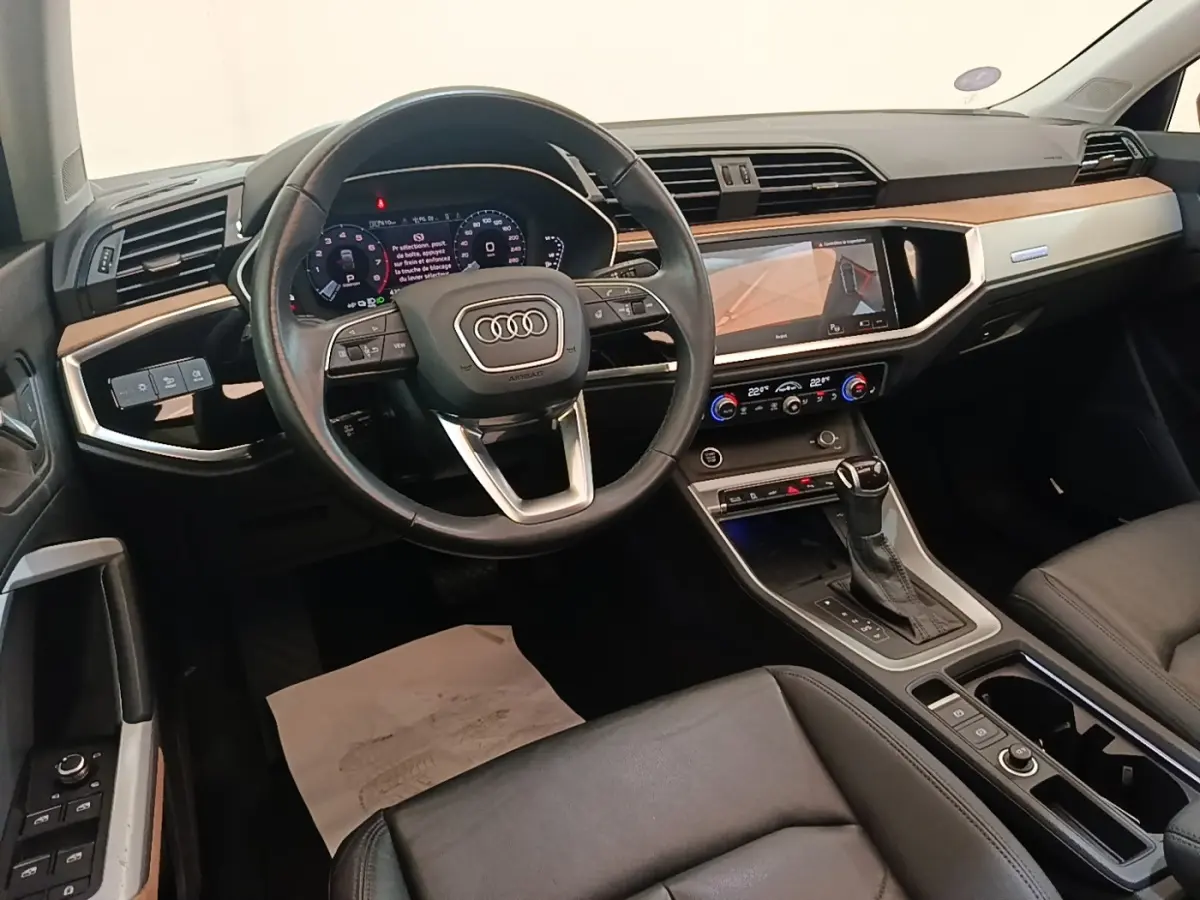 Intérieur Audi Q3 Sportback 2024 vu de face, volant cuir noir, tableau de bord avec écran tactile et inserts bois clair.