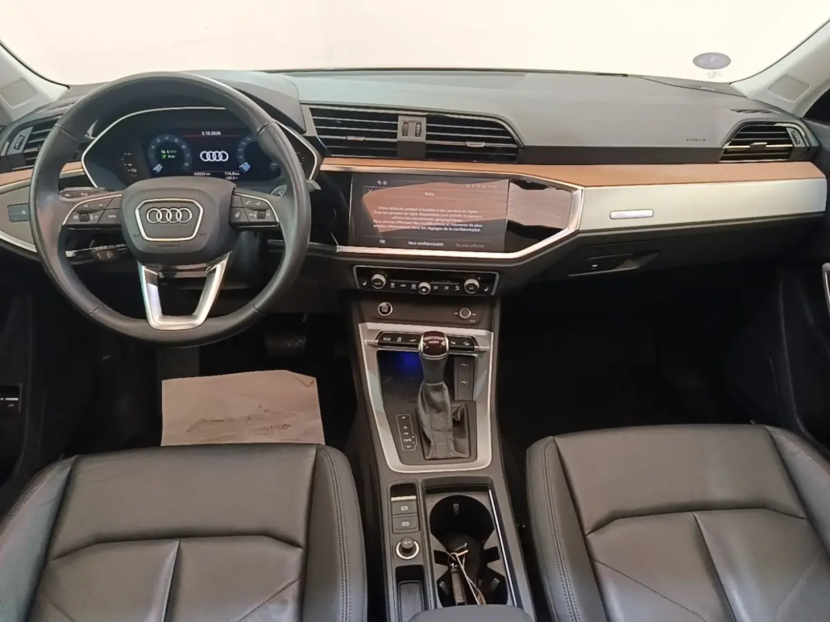 Vue intérieure avant de l'Audi Q3 Sportback 2024, tableau de bord noir avec inserts bois et écran tactile central.