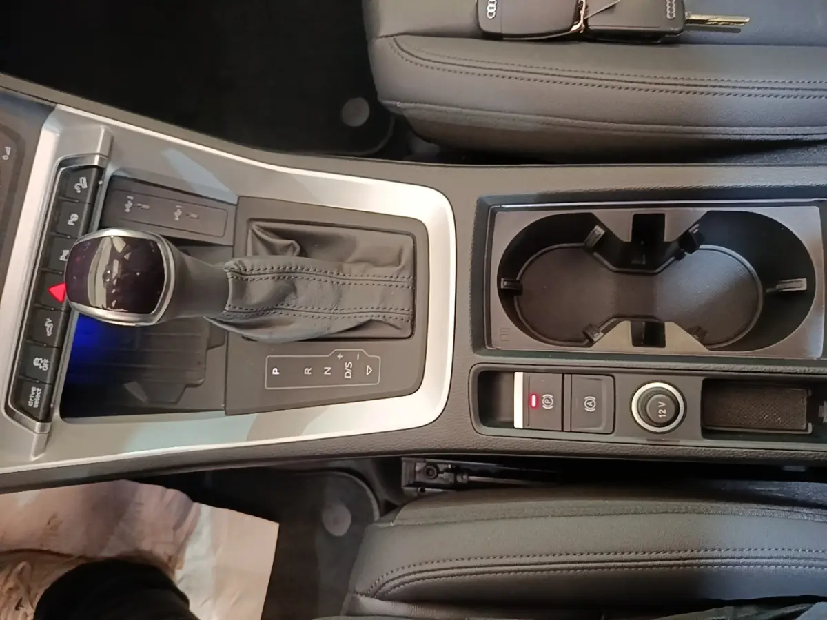 Vue rapprochée de la console centrale grise et noire de l’Audi Q3 Sportback 2024 avec levier de vitesses automatique et porte-gobelets.