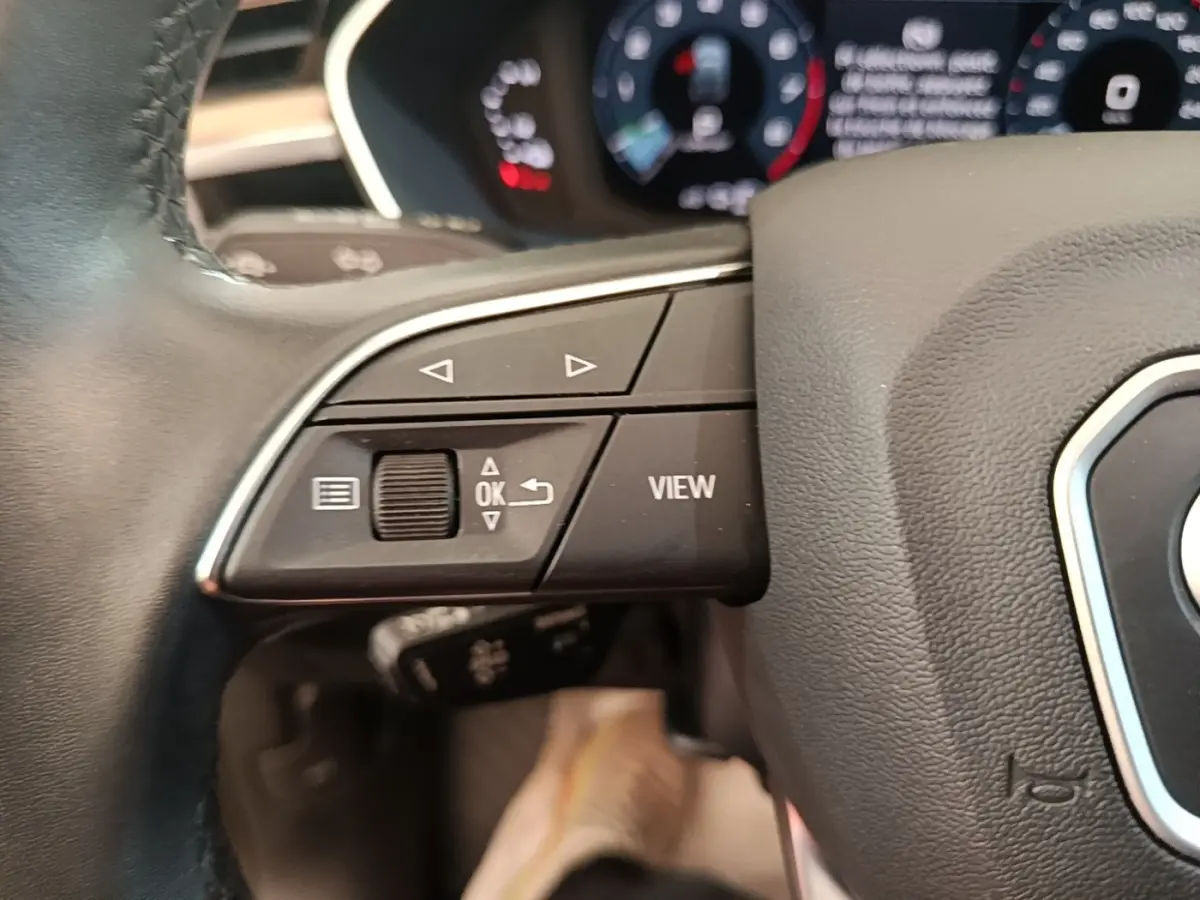 Gros plan sur les commandes gauche du volant noir d’un Audi Q3 Sportback 2024 avec affichage digital en arrière-plan.