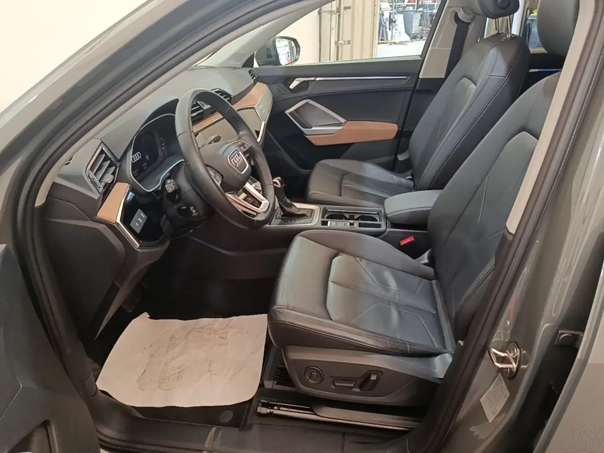 Vue intérieure côté conducteur de l'Audi Q3 Sportback 2024 avec sièges cuir noirs et tableau de bord gris et bois clair.