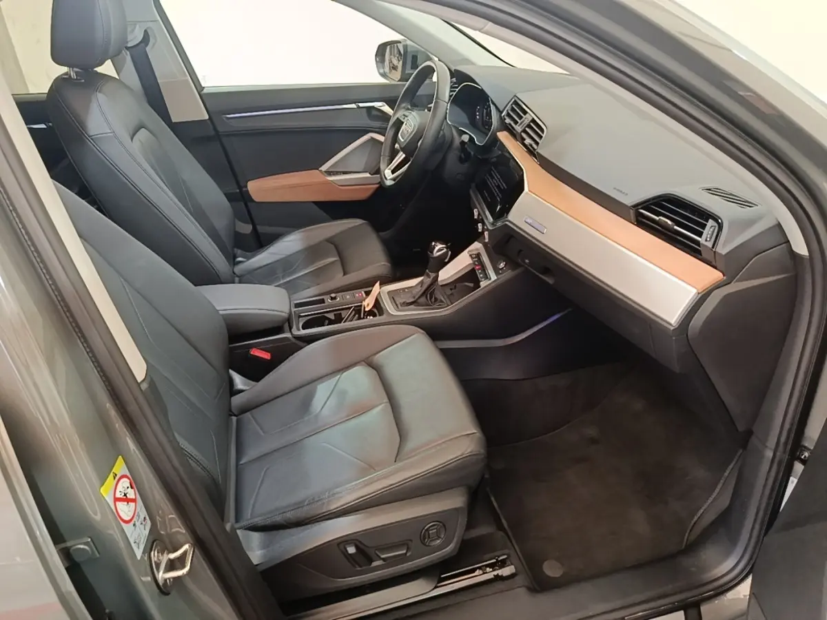 Vue intérieure côté conducteur de l'Audi Q3 Sportback 2024 avec sièges cuir noirs et tableau de bord bois clair.