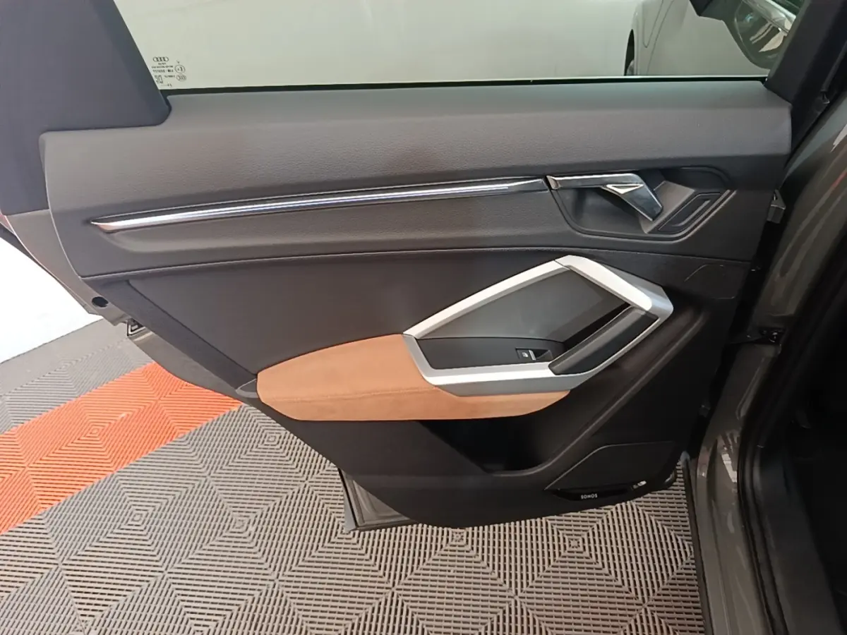 Vue rapprochée de la porte arrière droite de l'Audi Q3 Sportback 2024 avec garniture noire et accoudoir beige.