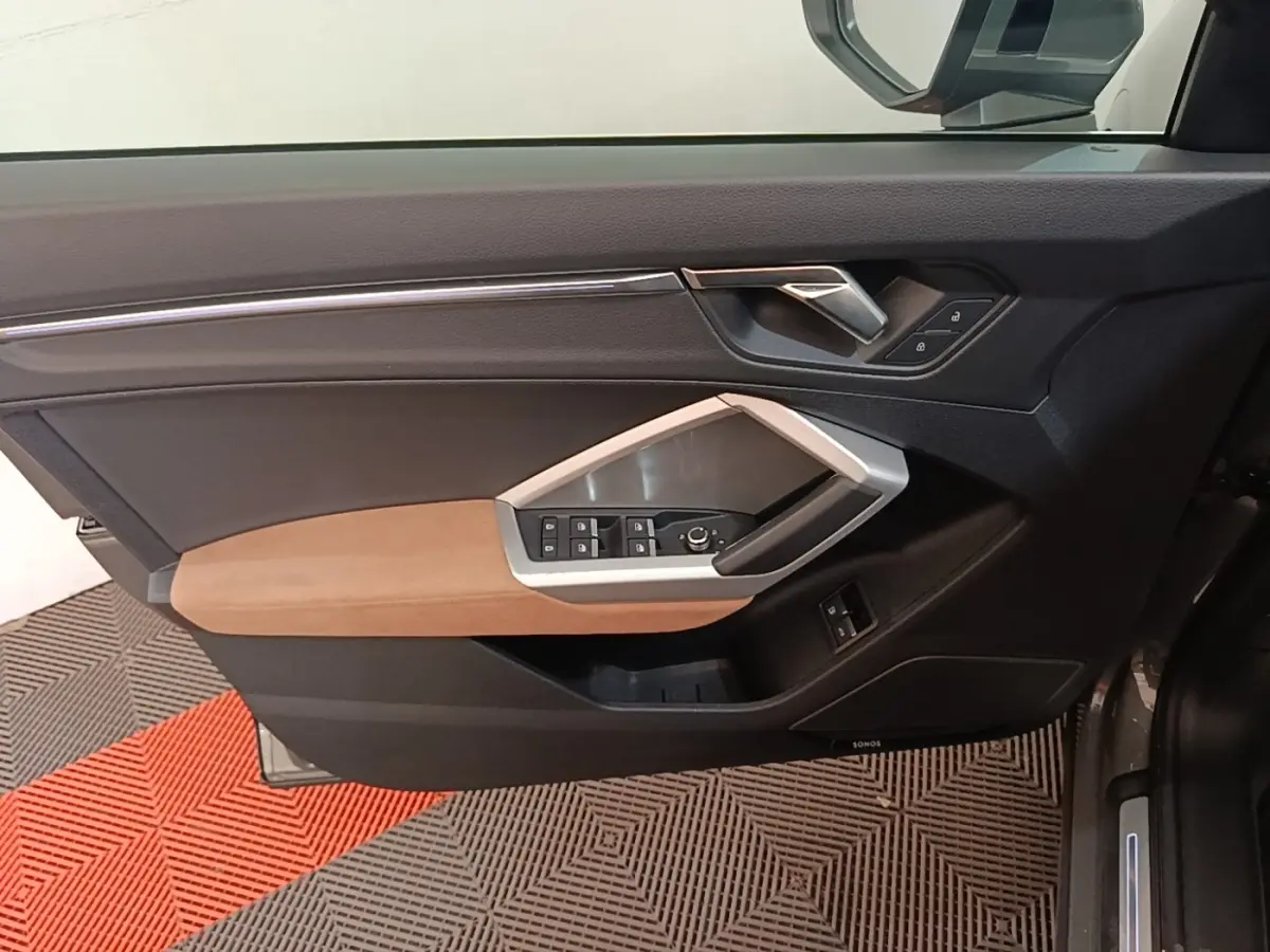 Vue intérieure côté gauche de la porte d'Audi Q3 Sportback 2024 avec garniture noire et accoudoir marron clair.