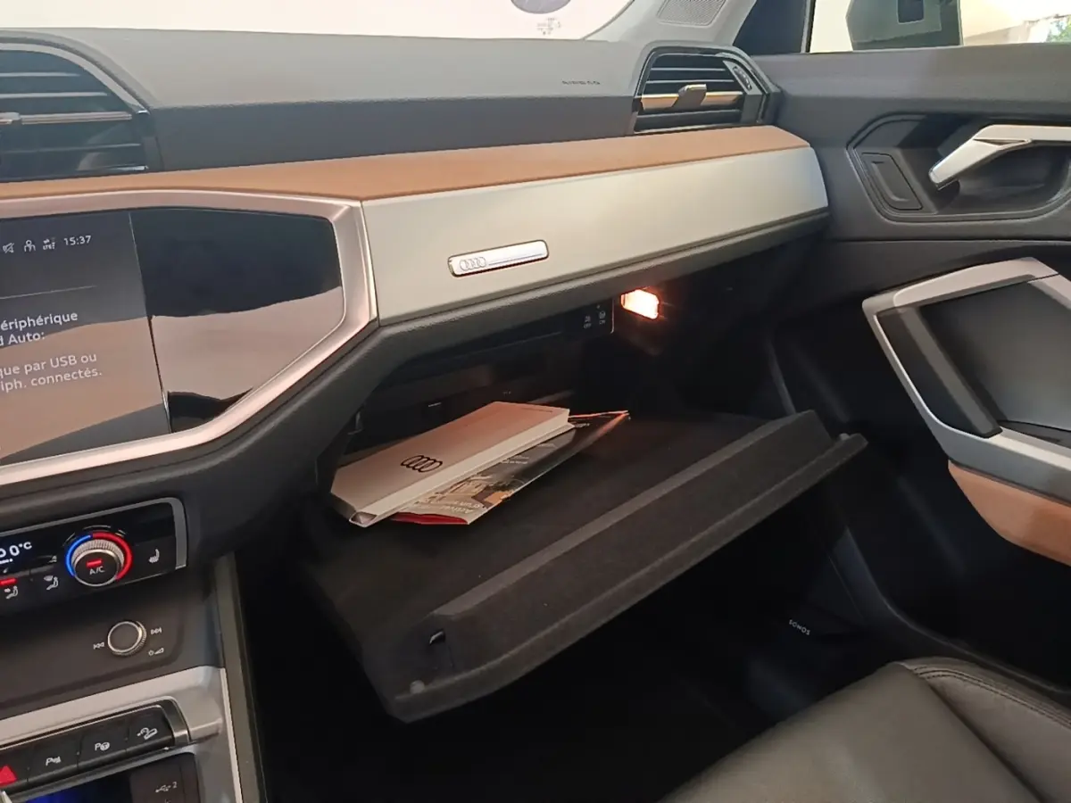Vue intérieure côté passager de l'Audi Q3 Sportback 2024 avec boîte à gants ouverte et tableau de bord bicolore beige et noir.
