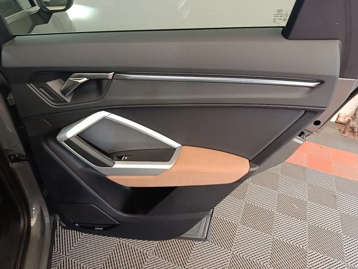 Vue intérieure côté gauche de la porte arrière d’un Audi Q3 Sportback 2024 avec garniture noire et insert marron clair.