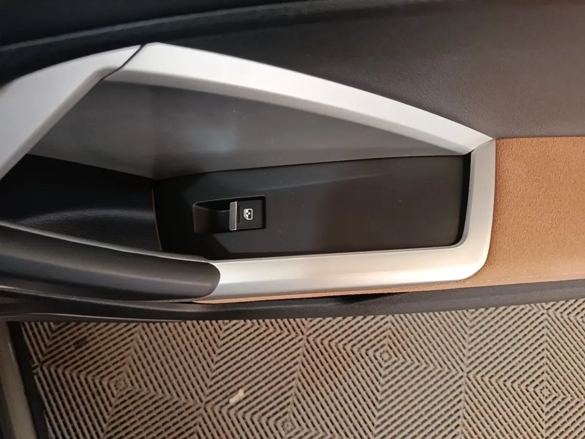Détail de la commande de lève-vitre sur la porte intérieure côté gauche, avec insert beige et noir.