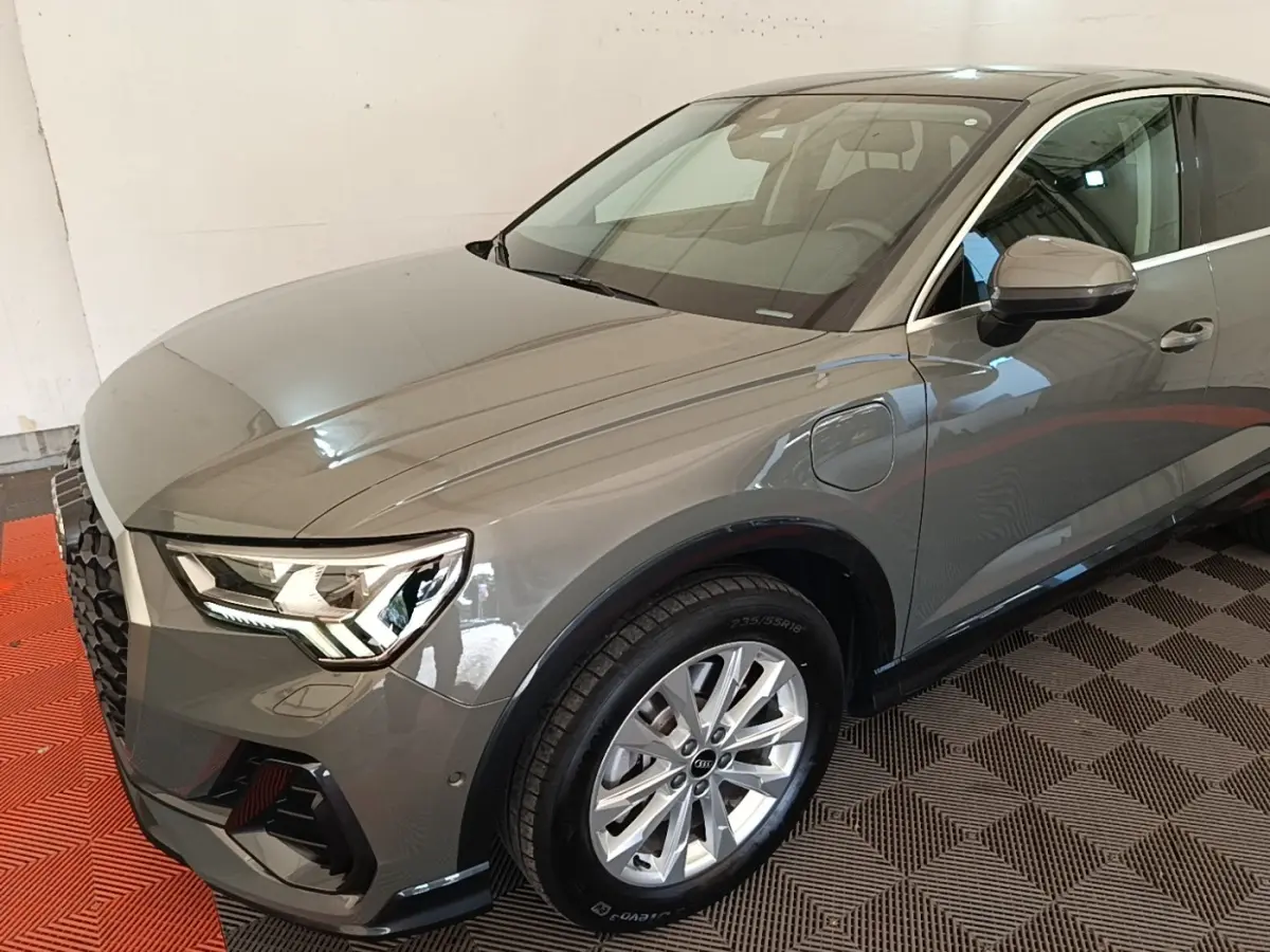 Audi Q3 Sportback gris métallisé vu en 3/4 avant droit, avec phares LED et jantes alliage visibles.