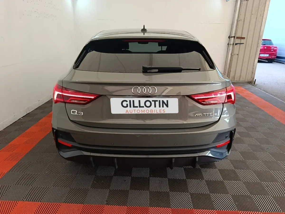 Vue arrière d'un Audi Q3 Sportback hybride rechargeable gris, avec feux LED allumés et logo distinctif sur coffre.