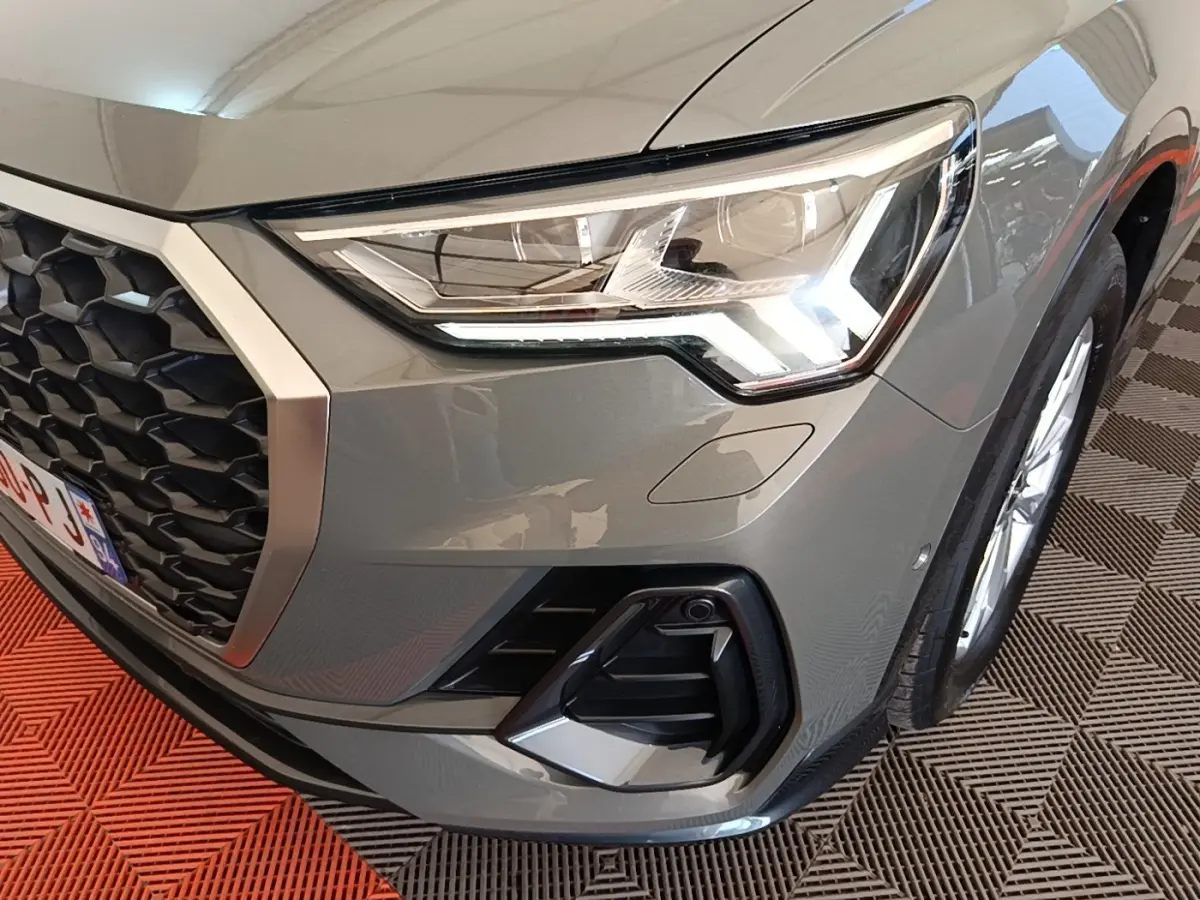 Gros plan sur l'avant droit gris d'un Audi Q3 Sportback 2024, mettant en valeur le phare LED et la calandre noire.