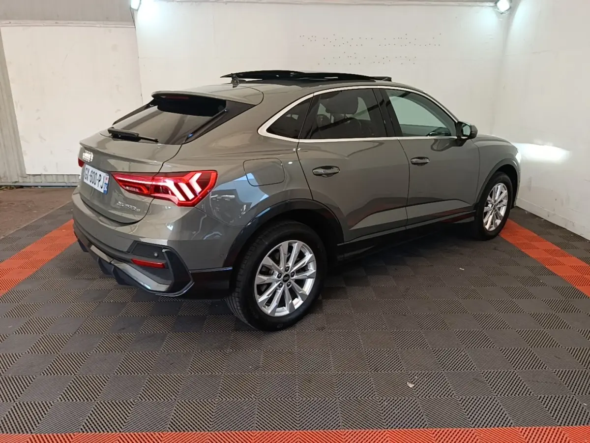 Audi Q3 Sportback gris vue 3/4 arrière droit, avec feux arrière LED allumés dans un garage.