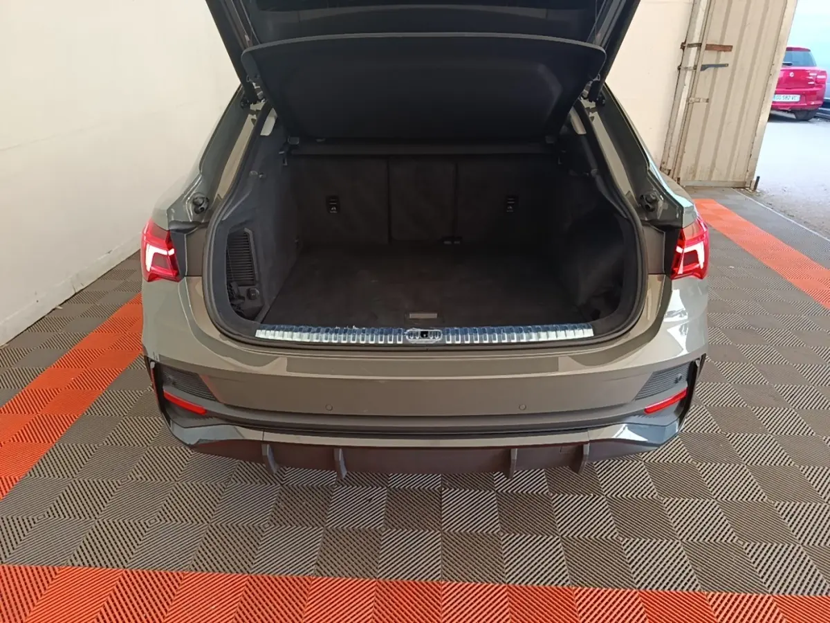 Vue arrière de l'Audi Q3 Sportback 2024 gris, coffre ouvert montrant l'espace de chargement vide et les feux arrière allumés.