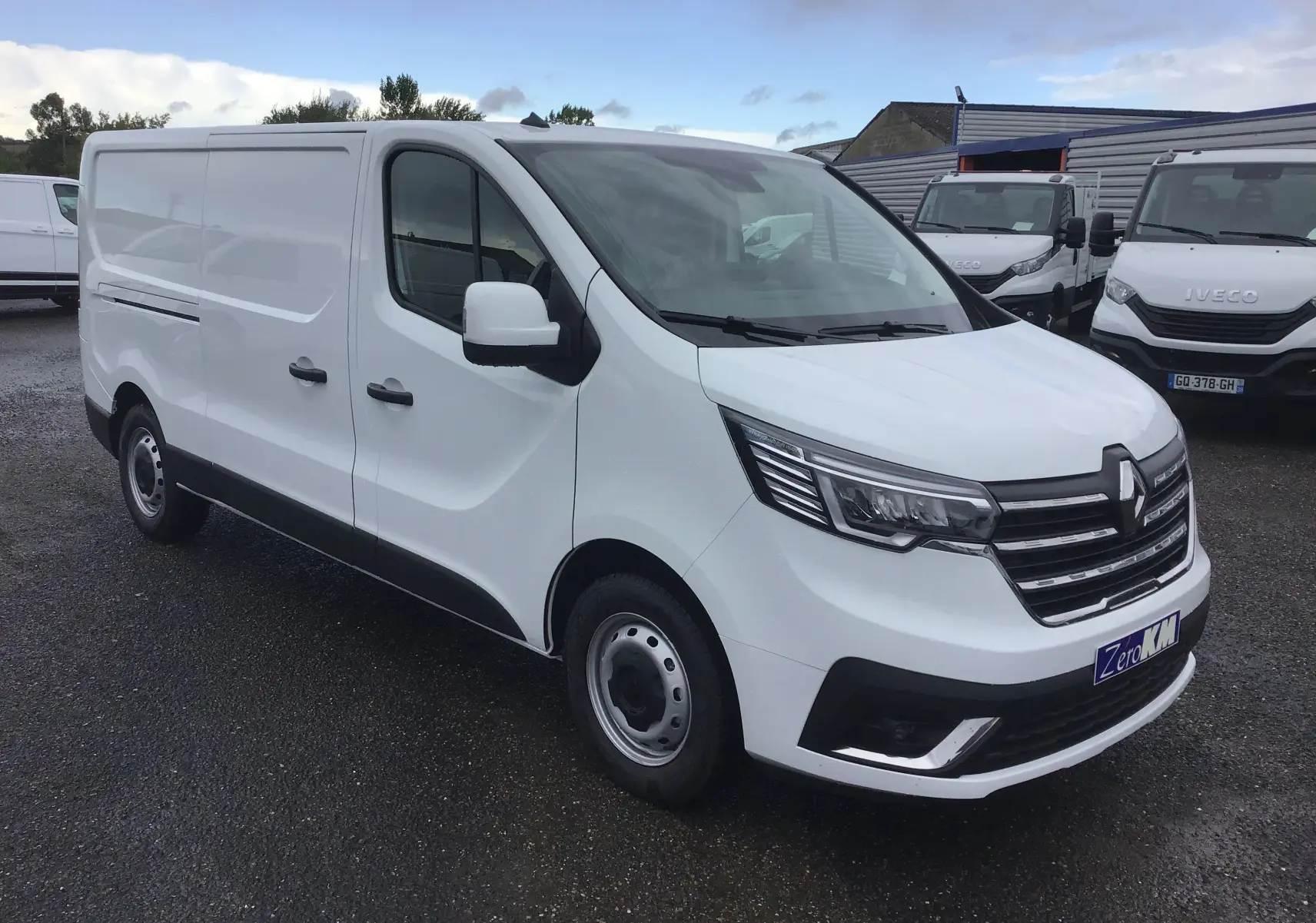 Renault Trafic Fourgon blanc en 3/4 avant droit, avec calandre noire et phares LED distinctifs.