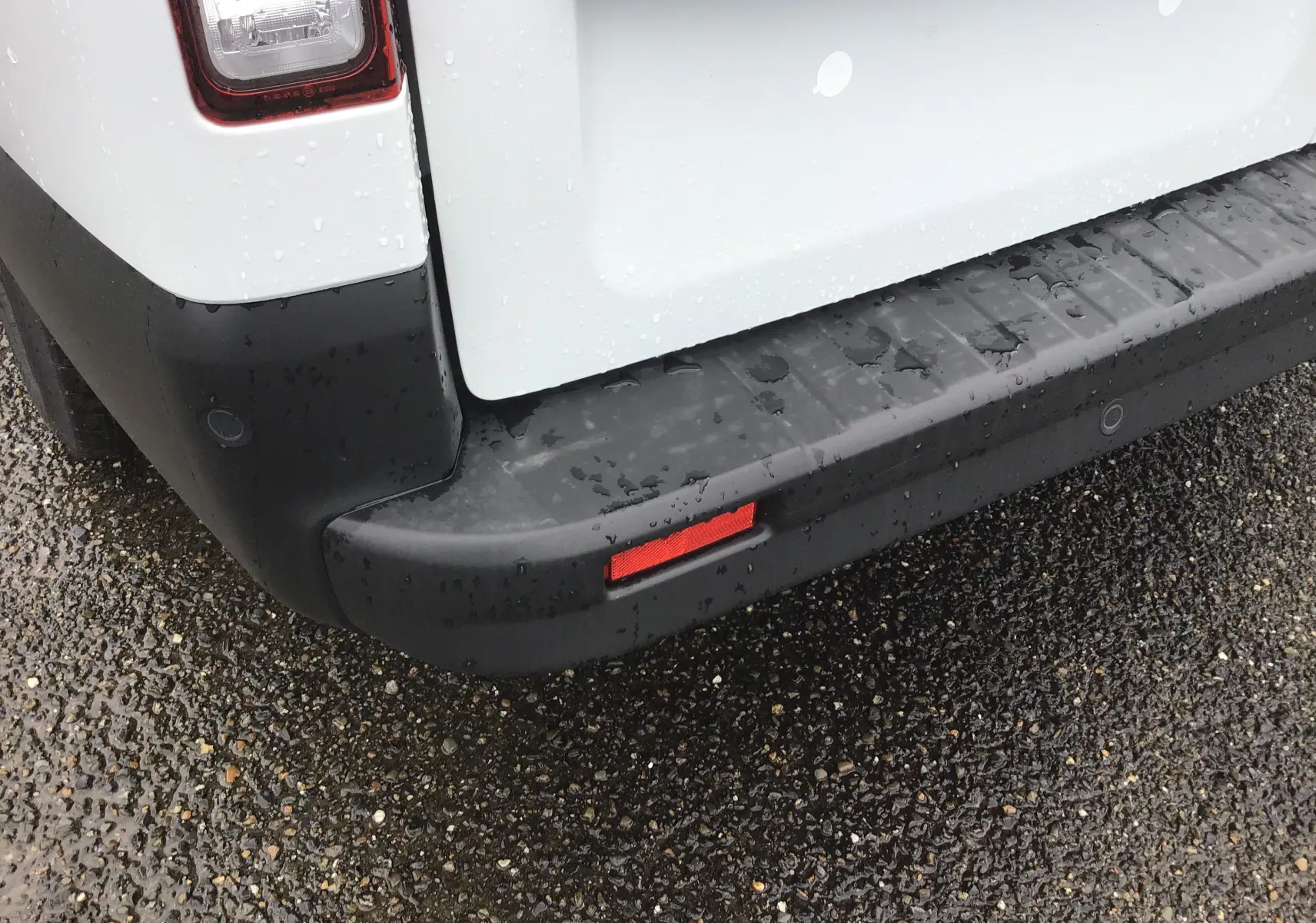 Gros plan sur le pare-chocs arrière noir et la partie blanche du coffre du Renault Trafic Fourgon L2H1 2023 sous la pluie.