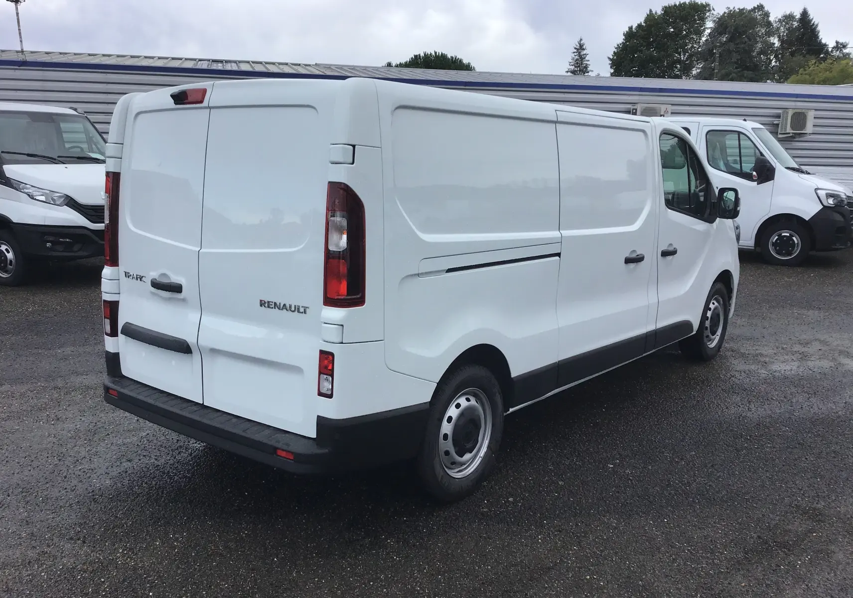 Vue 3/4 arrière droite d'un fourgon Renault Trafic blanc L2H1 2023 avec portes arrière fermées et jantes acier.