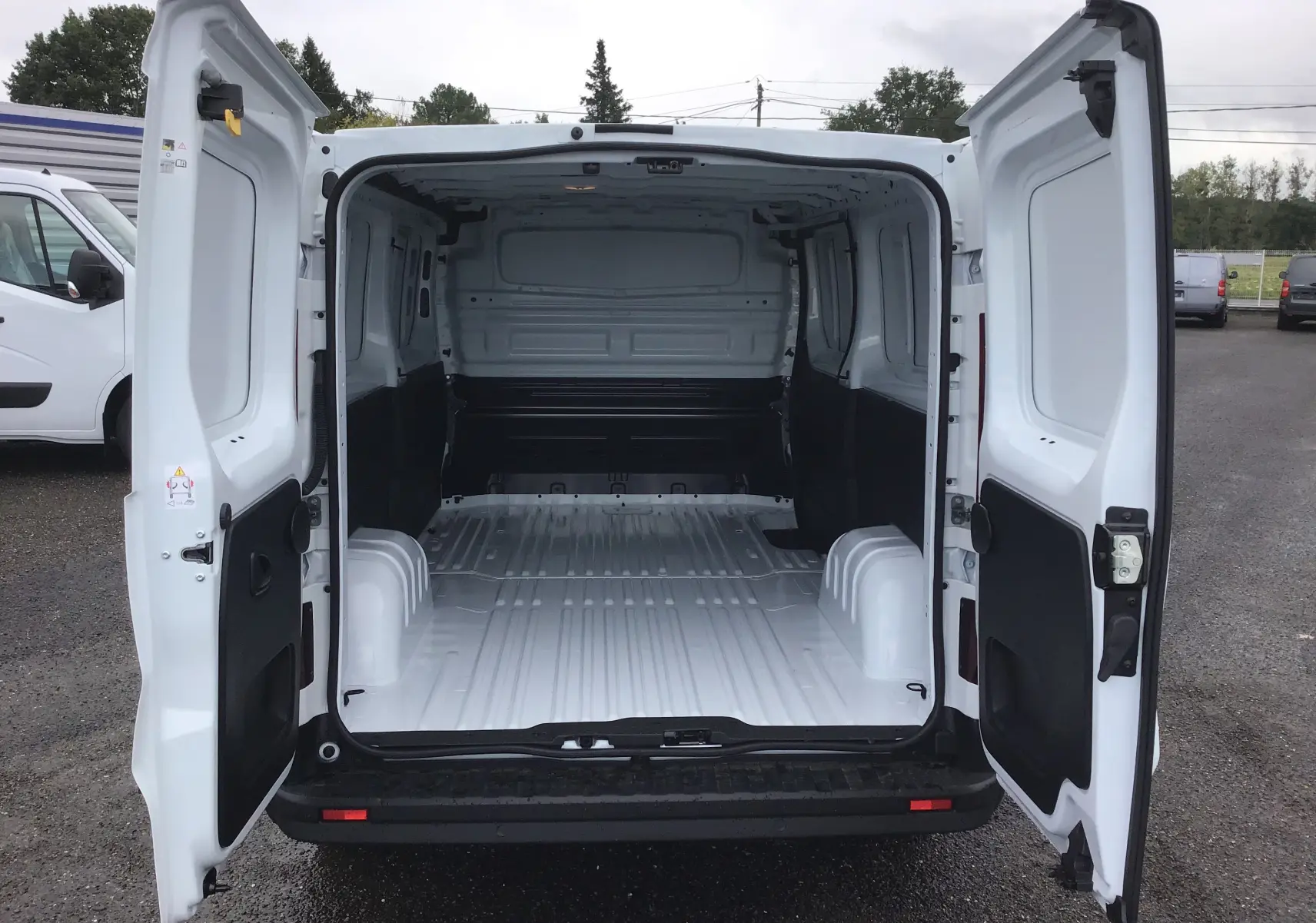 Vue arrière du Renault Trafic Fourgon blanc 2023 avec portes ouvertes montrant l'espace de chargement vide et spacieux.