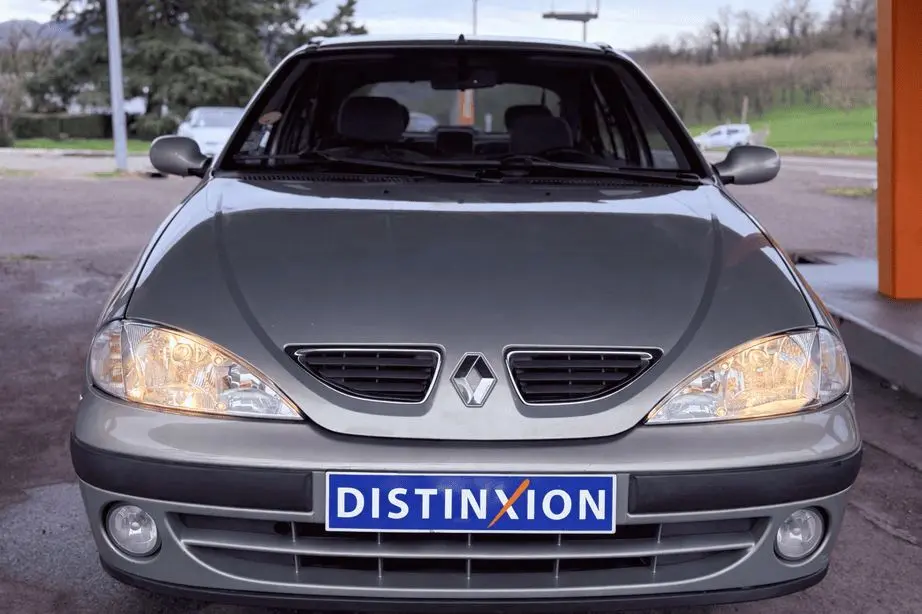 Vue frontale d'une Renault Mégane grise avec phares allumés et plaque d'immatriculation Distinxion visible.