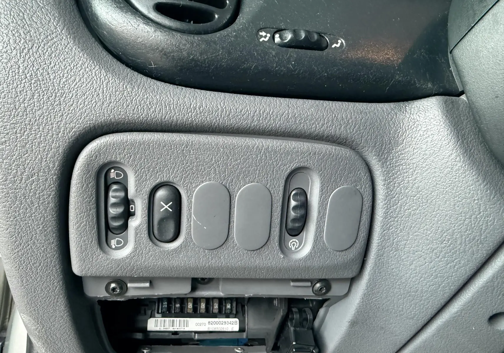 Gros plan sur les commandes grises du tableau de bord de la Renault Mégane, avec interrupteurs et boutons variés.