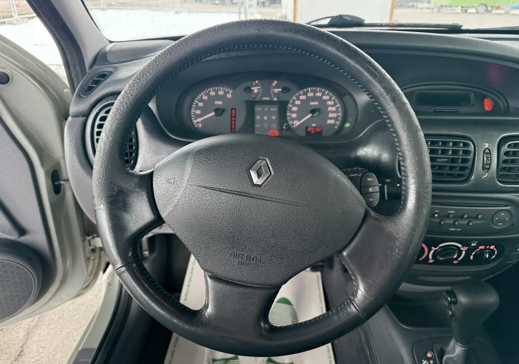 Vue intérieure centrée sur le volant en cuir noir d'une Renault Mégane 2000 avec tableau de bord et levier de boîte automatique.