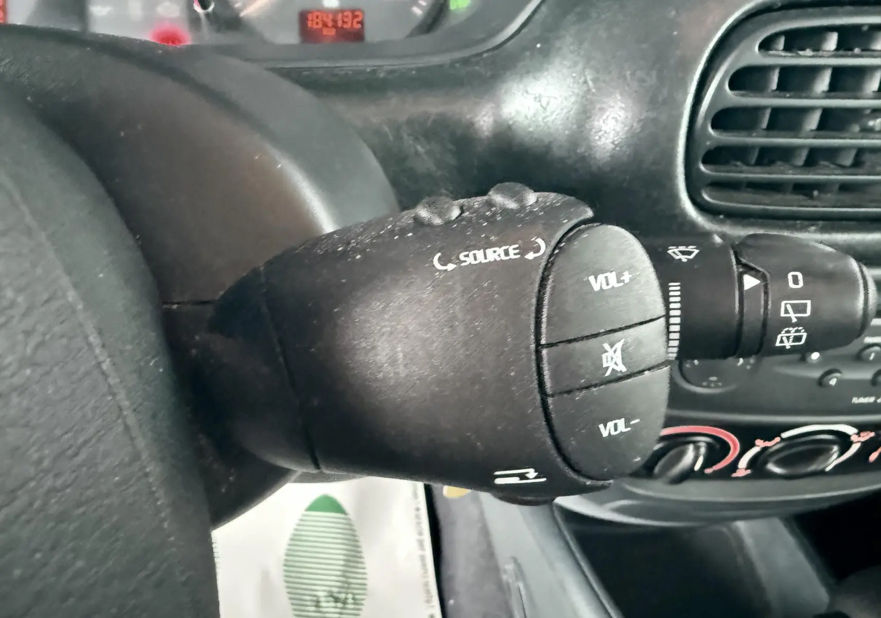 Gros plan sur la commande audio au volant d’une Renault Mégane verte, tableau de bord et aérateurs en arrière-plan.