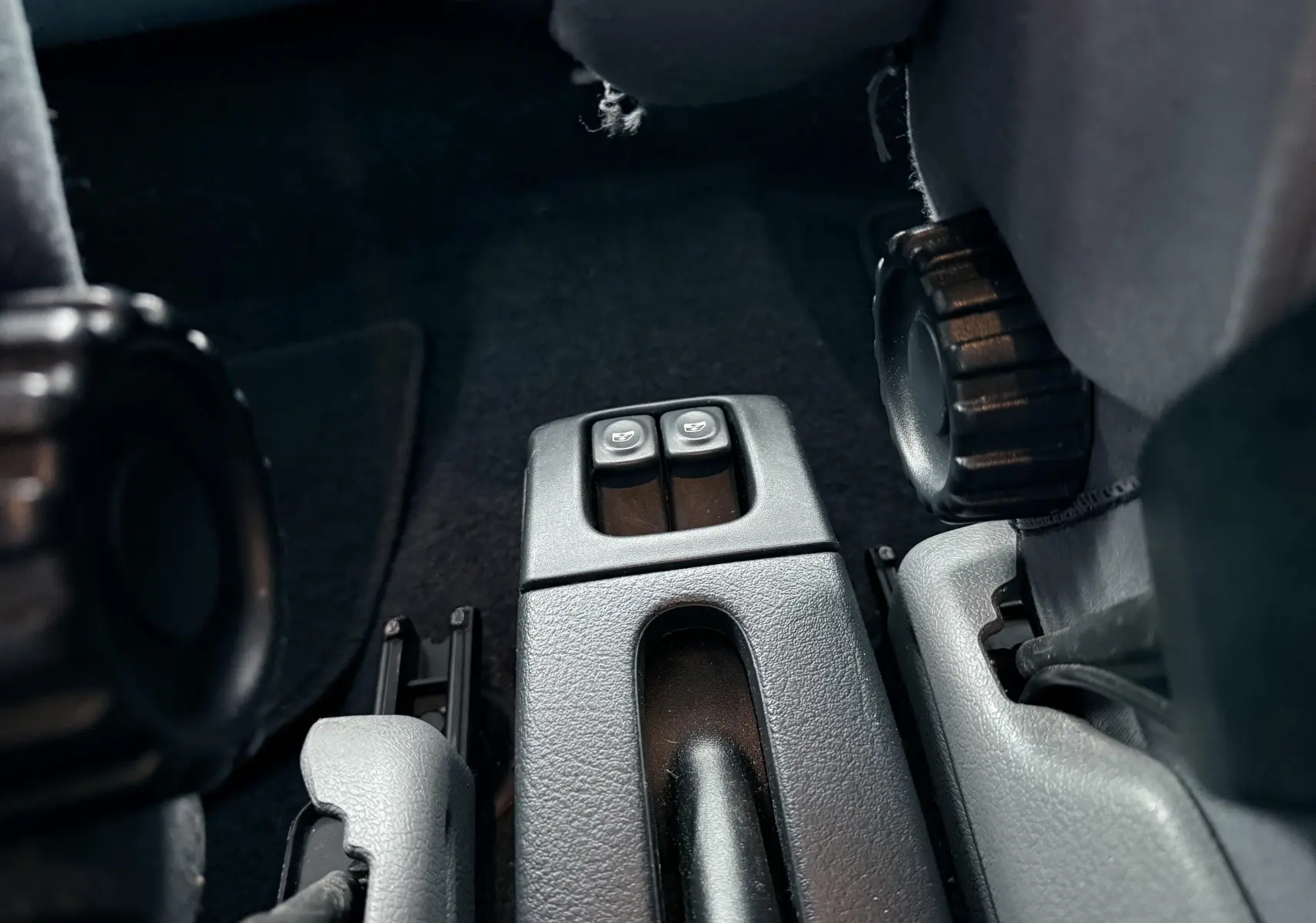 Gros plan sur les commandes de lève-vitres arrière entre les sièges avant d’une Renault Mégane verte de 2000.