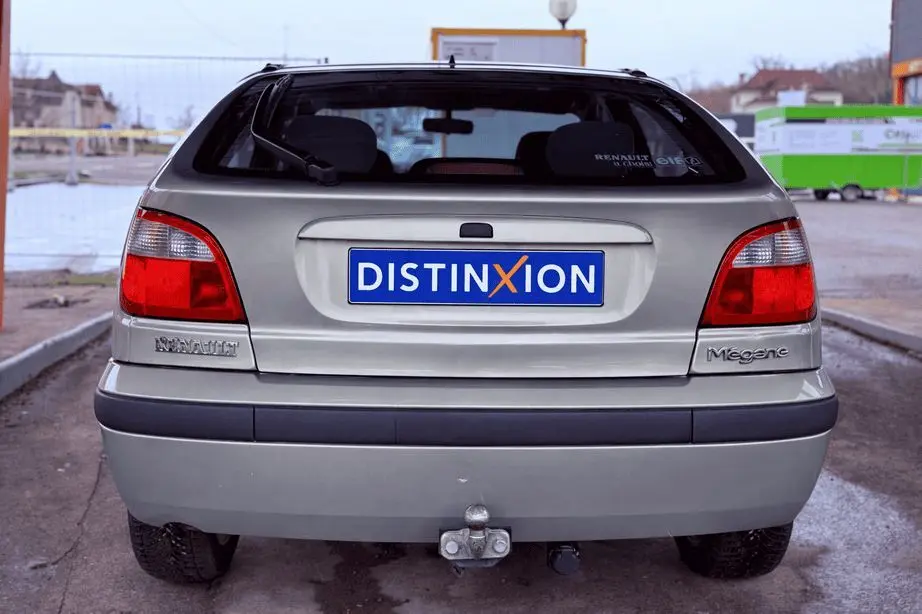 Vue arrière d'une Renault Mégane verte de 2000 avec attelage et plaque Distinxion visible.