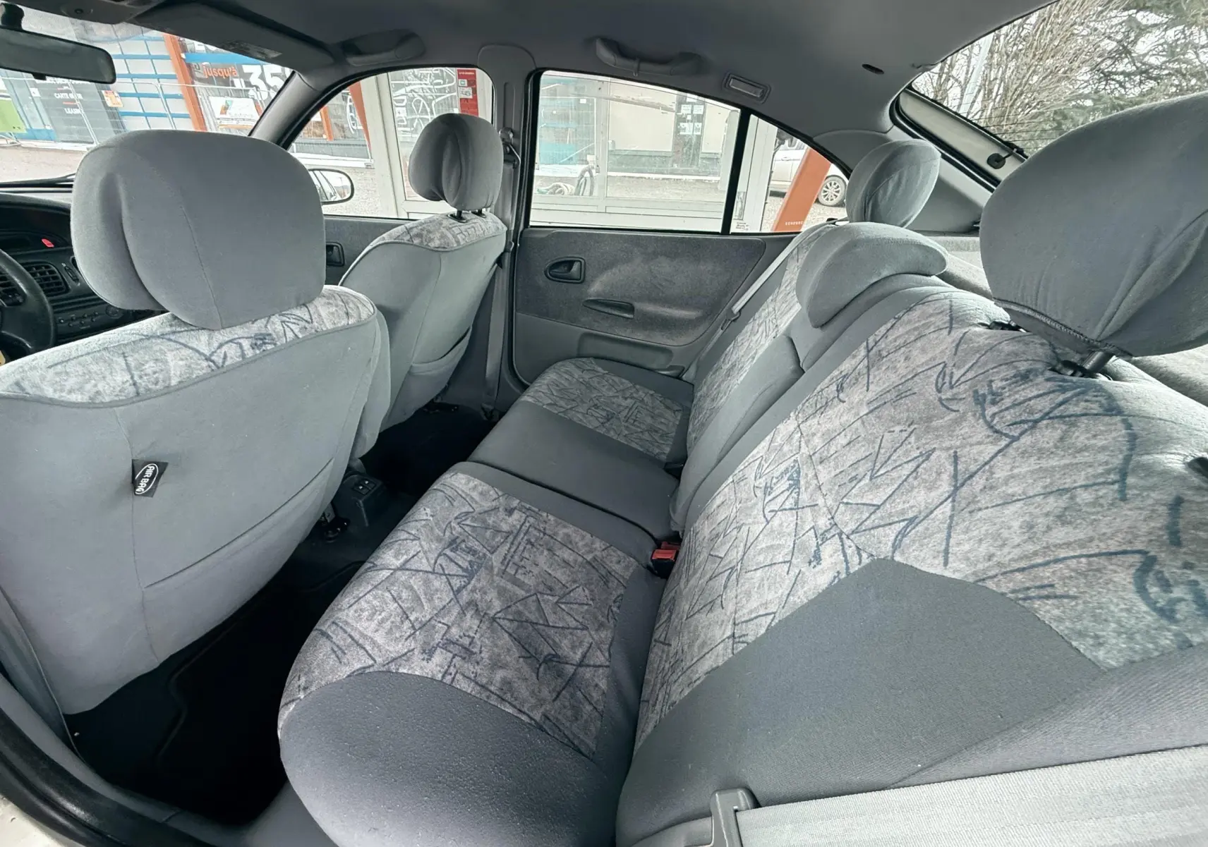 Vue intérieure arrière côté droit montrant les sièges tissu gris à motifs de la Renault Mégane 2000.