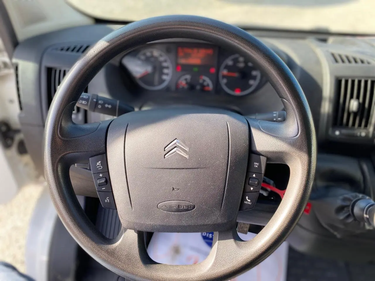 Volant noir de Citroën Jumper 2013 vu de face, avec commandes intégrées et tableau de bord flou en arrière-plan.