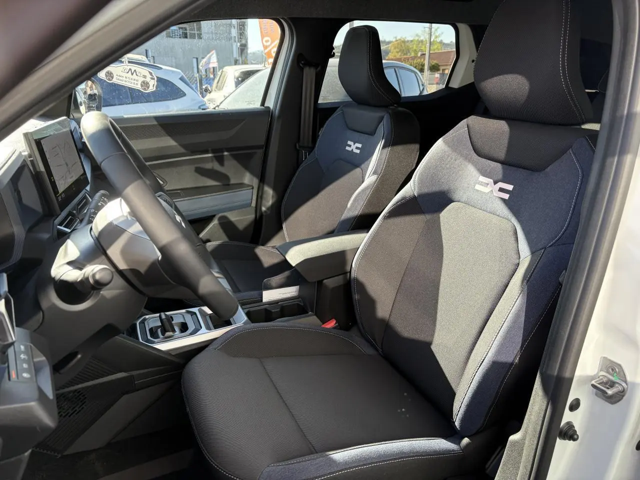 Intérieur du Dacia Duster blanc 2024, vue côté conducteur, sièges en tissu Denim bleu avec logo Dacia.