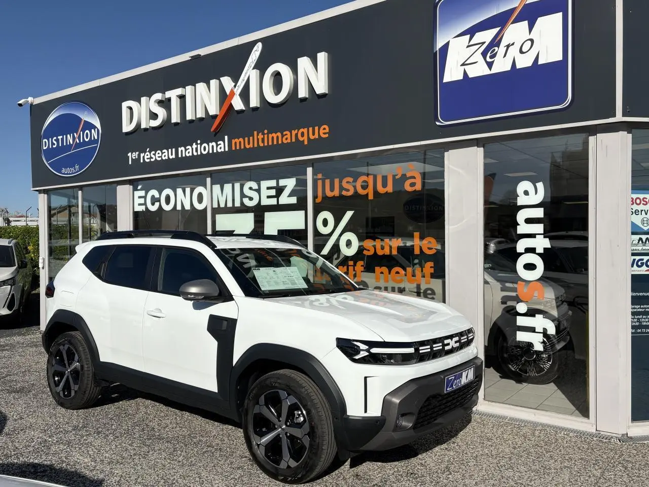 SUV Dacia Duster blanc métallisé vu de 3/4 avant droit, avec jantes alliage noires et barres de toit noires.