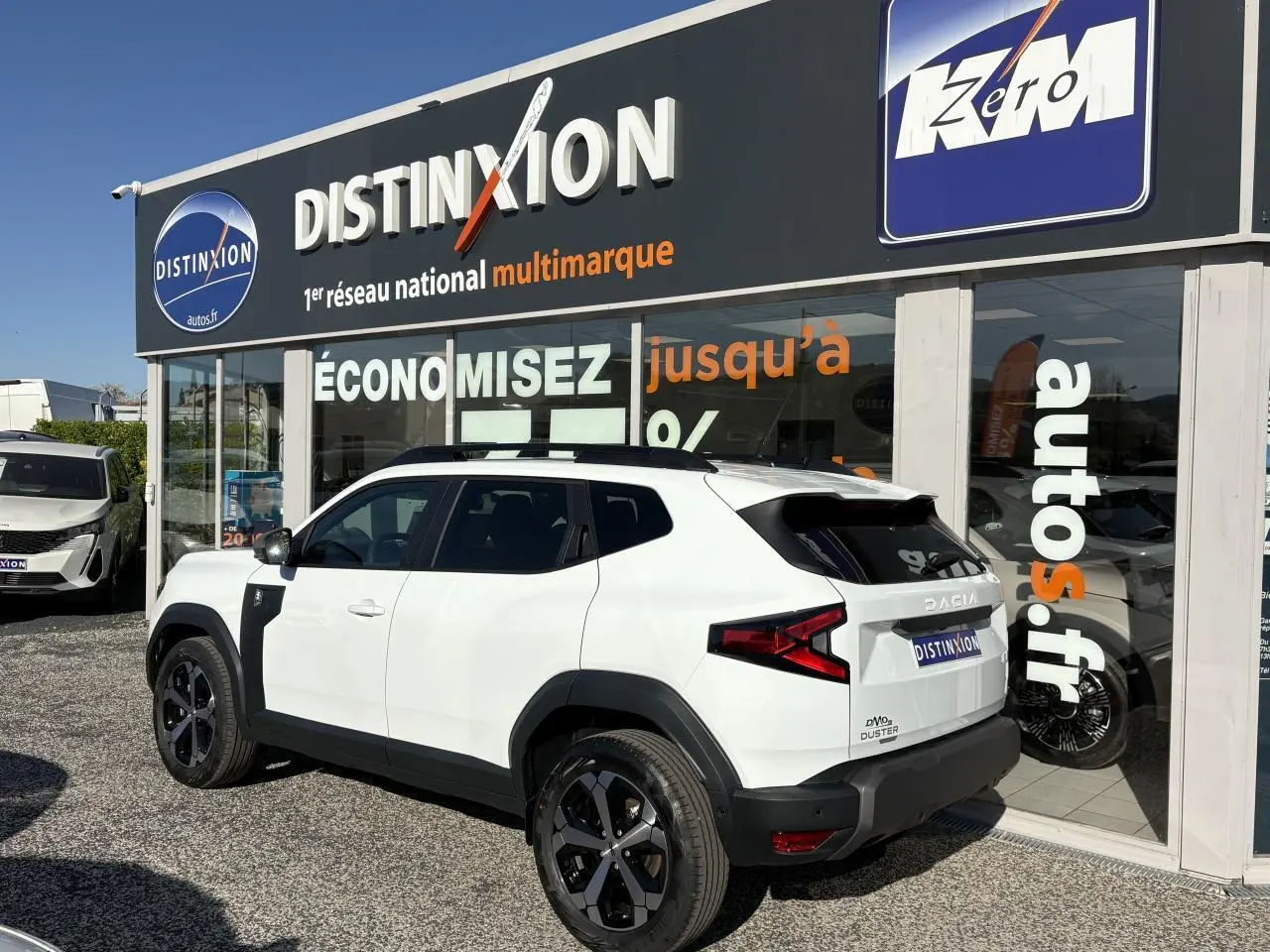 Vue 3/4 arrière droite du Dacia Duster 1.6 Hybrid blanc métallisé avec barres de toit noires et jantes alliage 18 pouces.