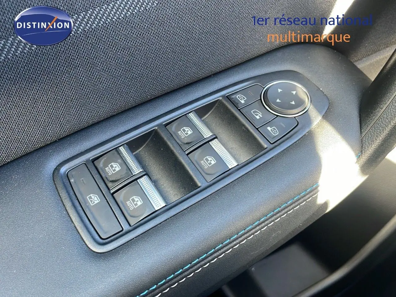 Gros plan sur les commandes des vitres électriques côté conducteur du Renault Captur gris Rafale métal avec surpiqûres bleues.