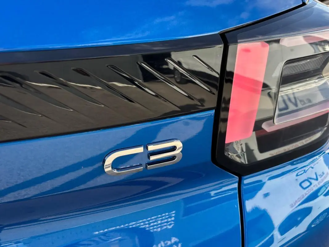 Gros plan sur le logo C3 et le feu arrière droit d'une Citroën C3 bleu vif, soulignant le bandeau noir décoratif.