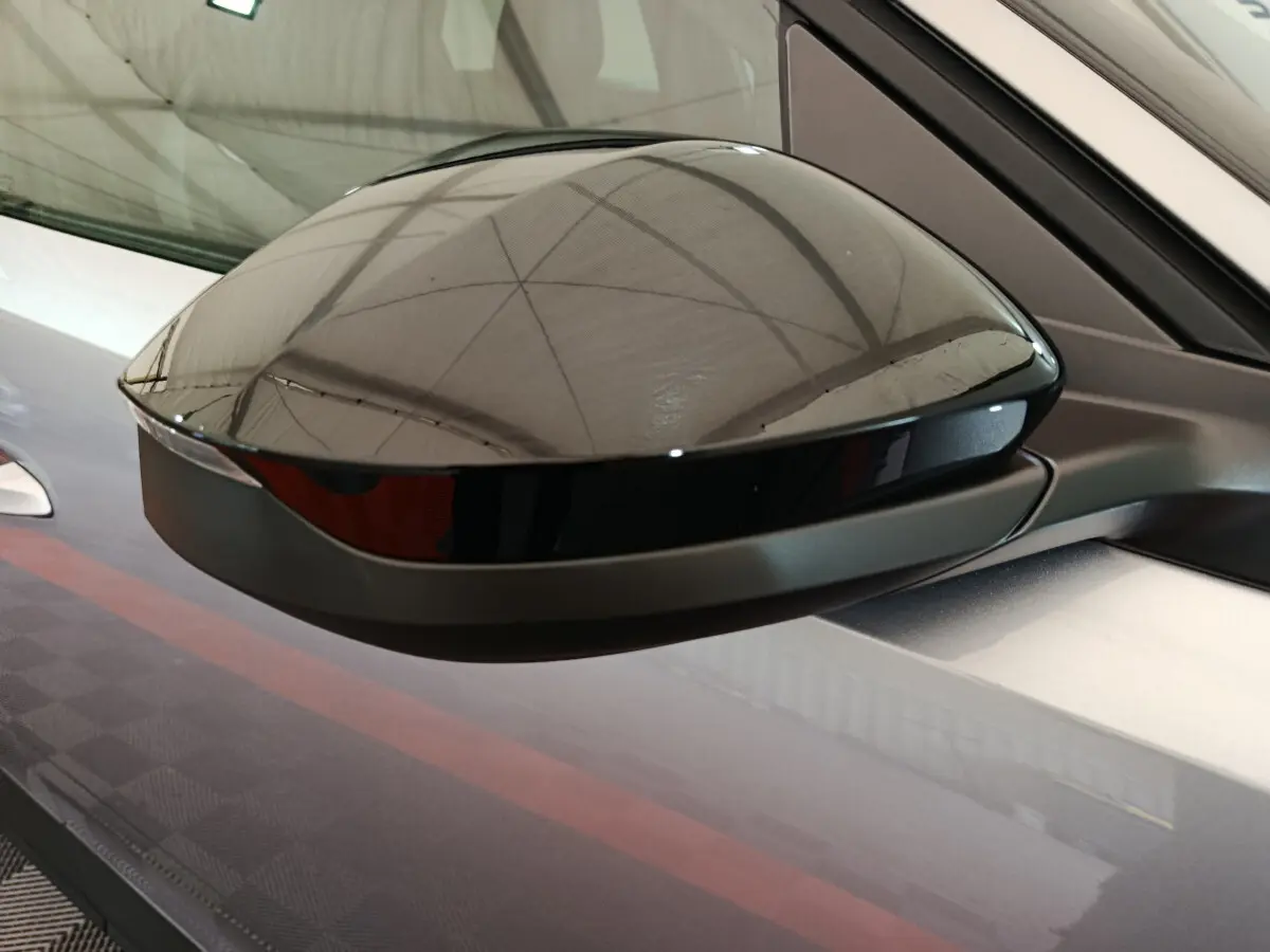 Rétroviseur noir brillant côté gauche sur Peugeot 3008 gris clair, vue rapprochée en intérieur d'atelier.