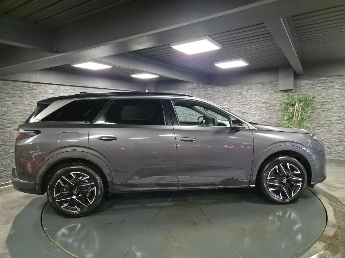 Profil droit d'un Peugeot 5008 gris métallisé 2025 avec jantes alliage noires et toit noir en intérieur showroom.