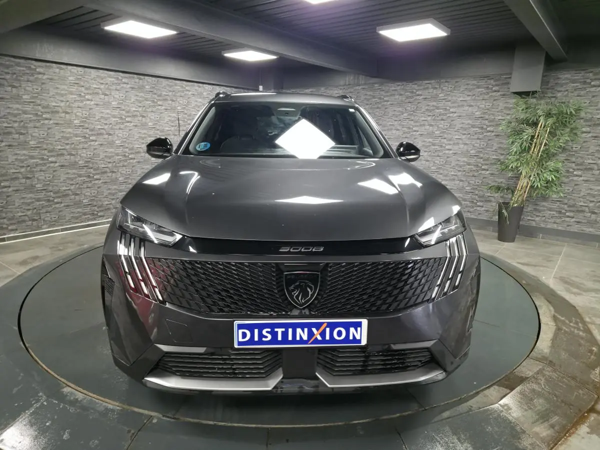 Vue frontale d'un Peugeot 5008 gris métallisé 2025 avec calandre noire et feux LED à griffes dans un showroom.