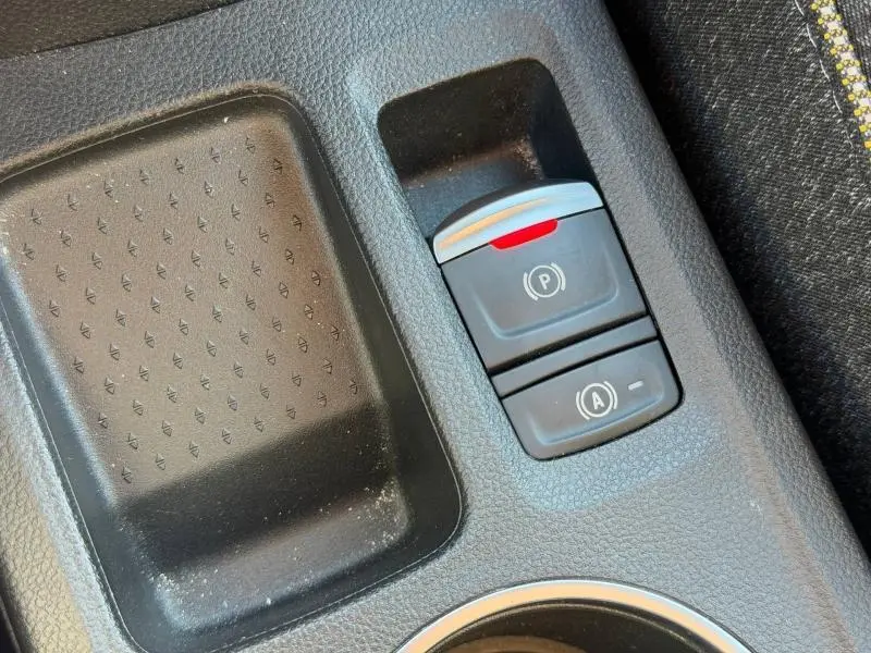 Gros plan sur la console centrale du Renault Captur 2025 rouge, montrant les boutons du frein à main électrique et du système start-stop.
