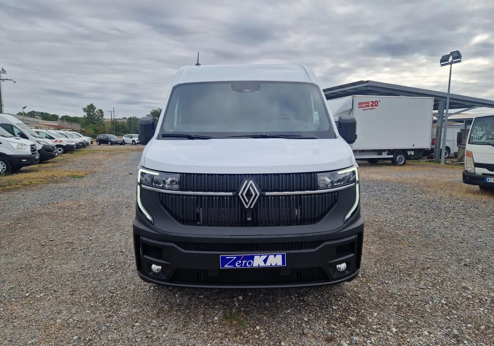 Vue frontale d’un Renault Master blanc 2026 avec calandre noire et feux LED en forme de C, sur parking extérieur.