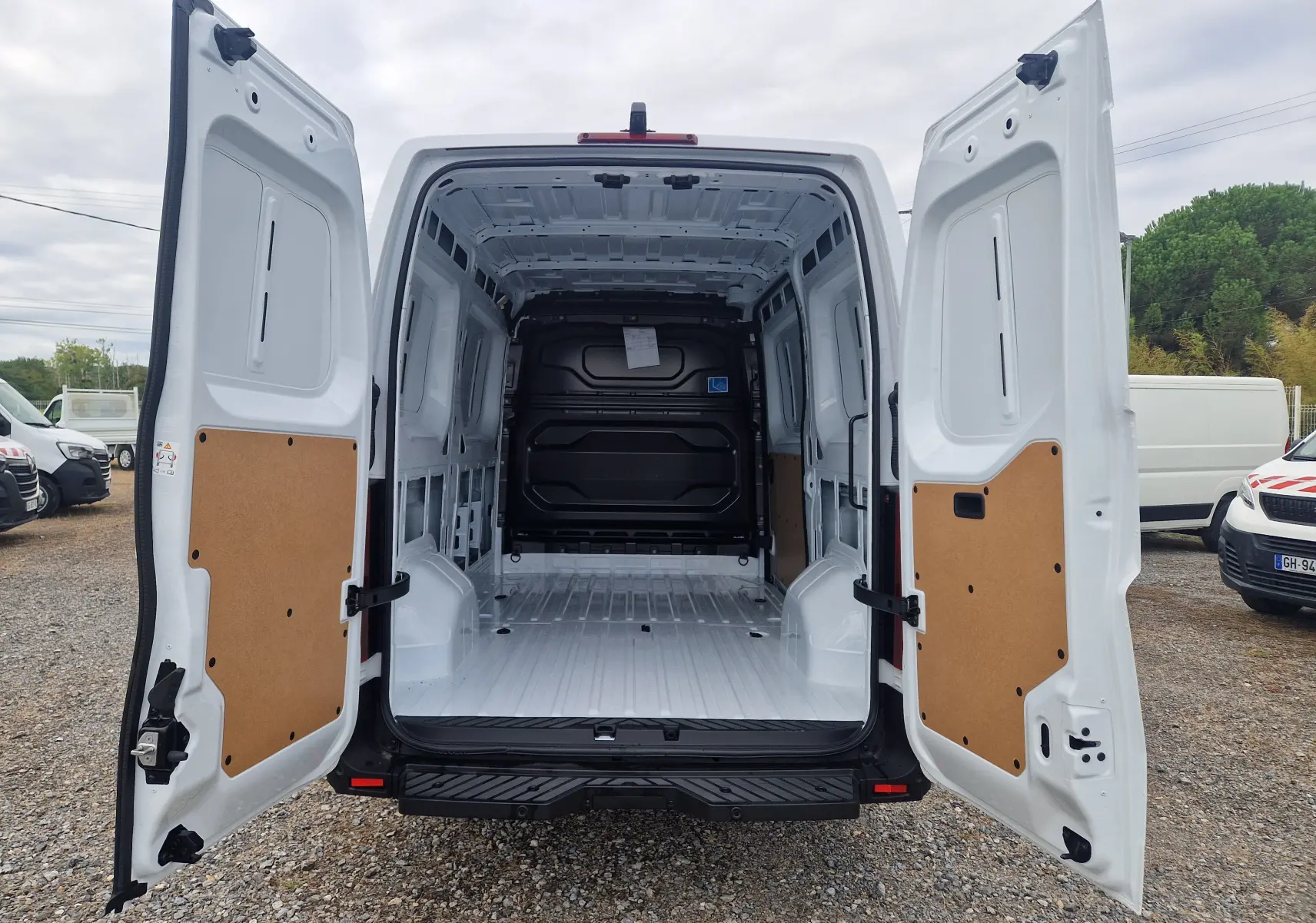 Vue arrière d’un Renault Master blanc 2026 avec portes ouvertes montrant un espace de chargement vide et protégé par des panneaux en bois.